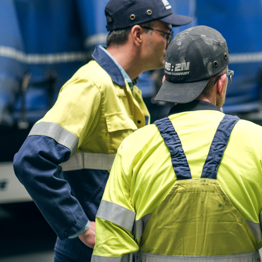 Two REAZN employees in discussion wearing safety gear, collaborating on zinc alloy production